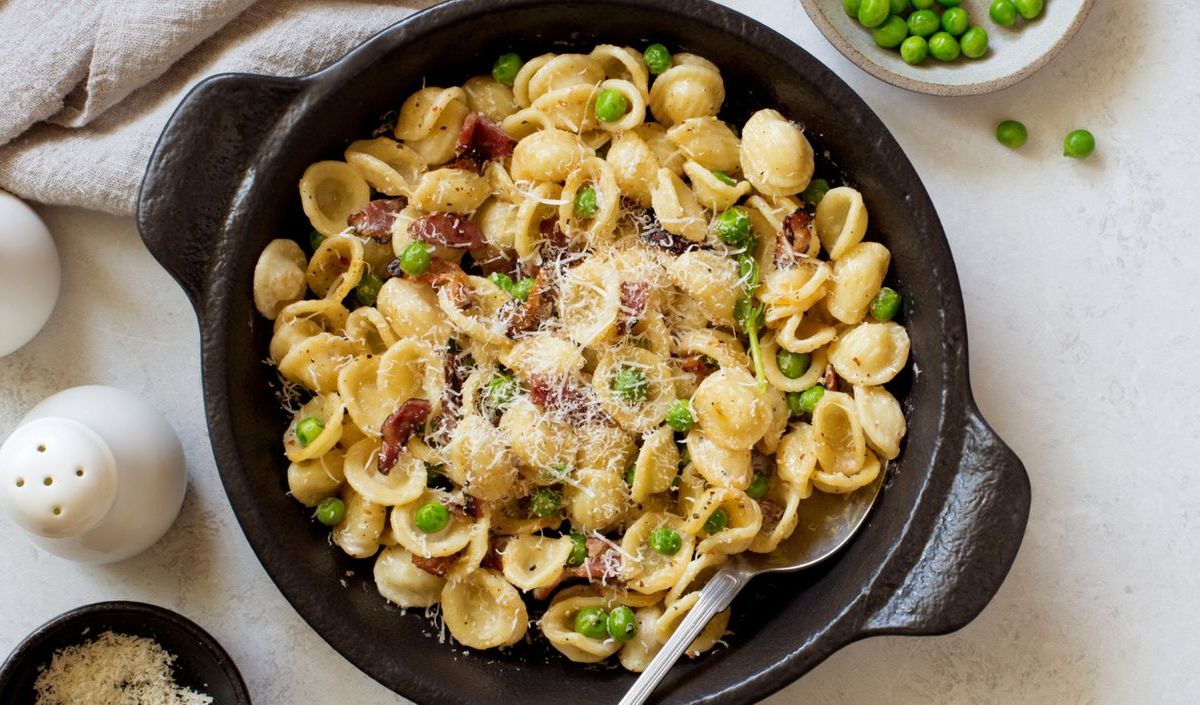 Nudeln mit Erbsen, Speck und Parmesan in einer schwarzen Gusseisenpfanne.