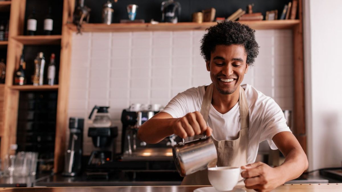 Barista bereitet lächelnd einen Cappuccino vor