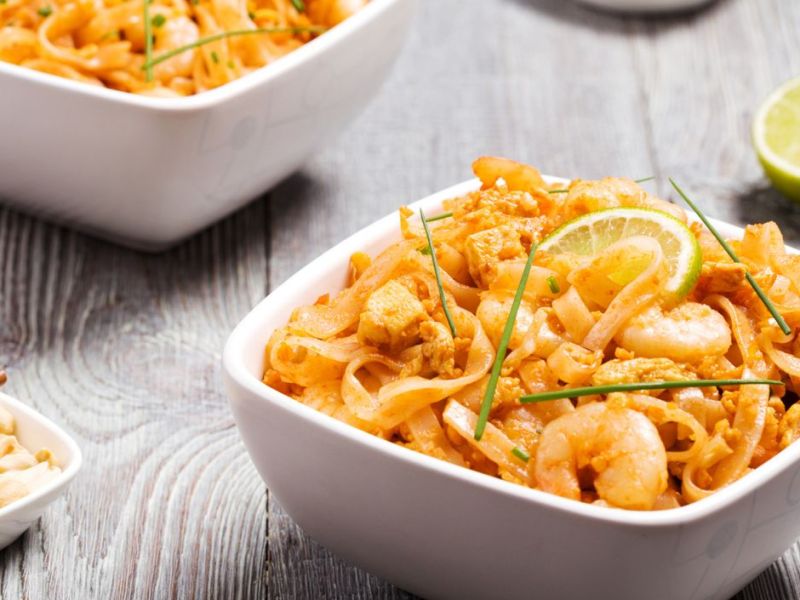 Pad Thai mit Shrimps und Limetten in weißen Schüsseln.