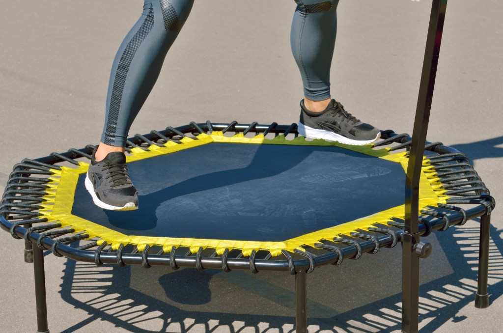 Man sieht die Beine einer Frau in Sportkleidung, die auf einem Jumping Fitness Trampolin springt.