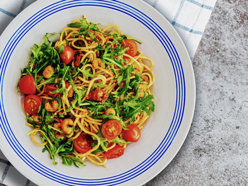 Spaghetti mit Rucola und Tomaten auf einem weißen Teller mit blauem Rand
