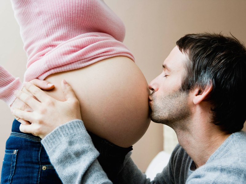 Mann küsst Babybauch seiner Frau