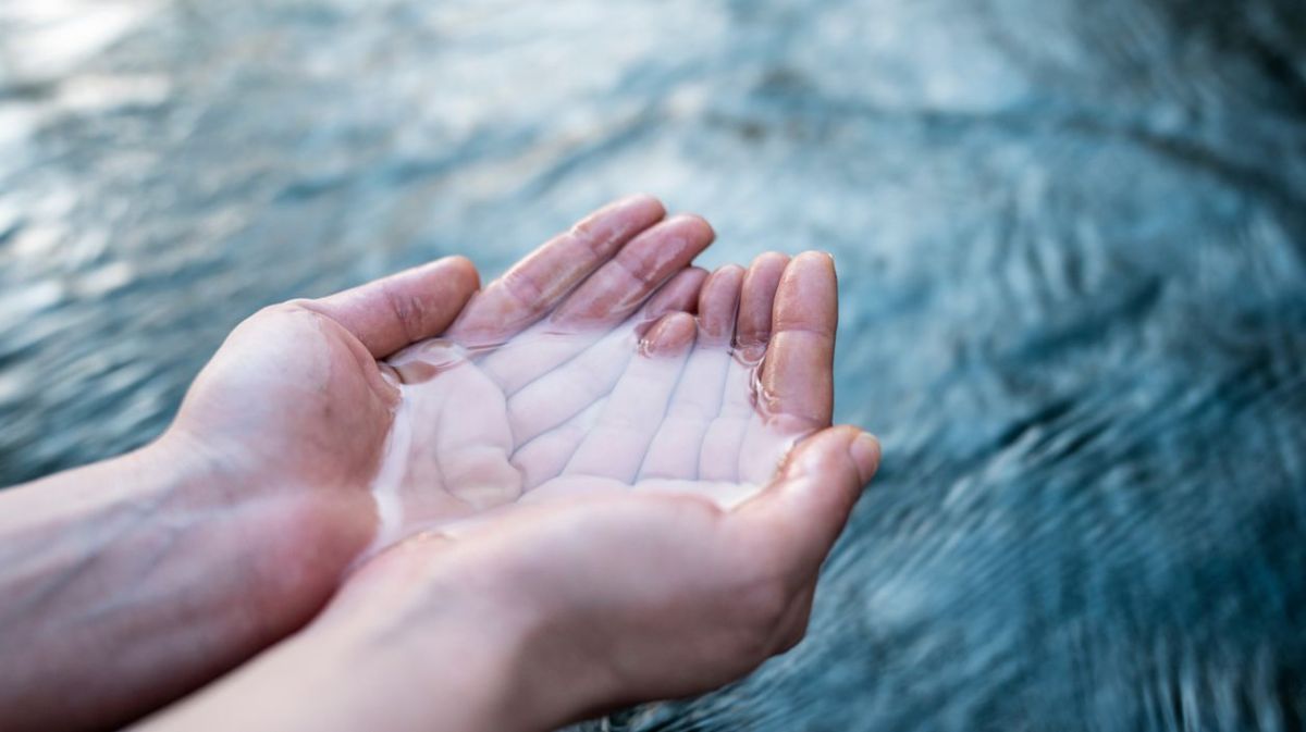 Wasser in zusammengehaltenen Händen über einem fließenden Strom. 