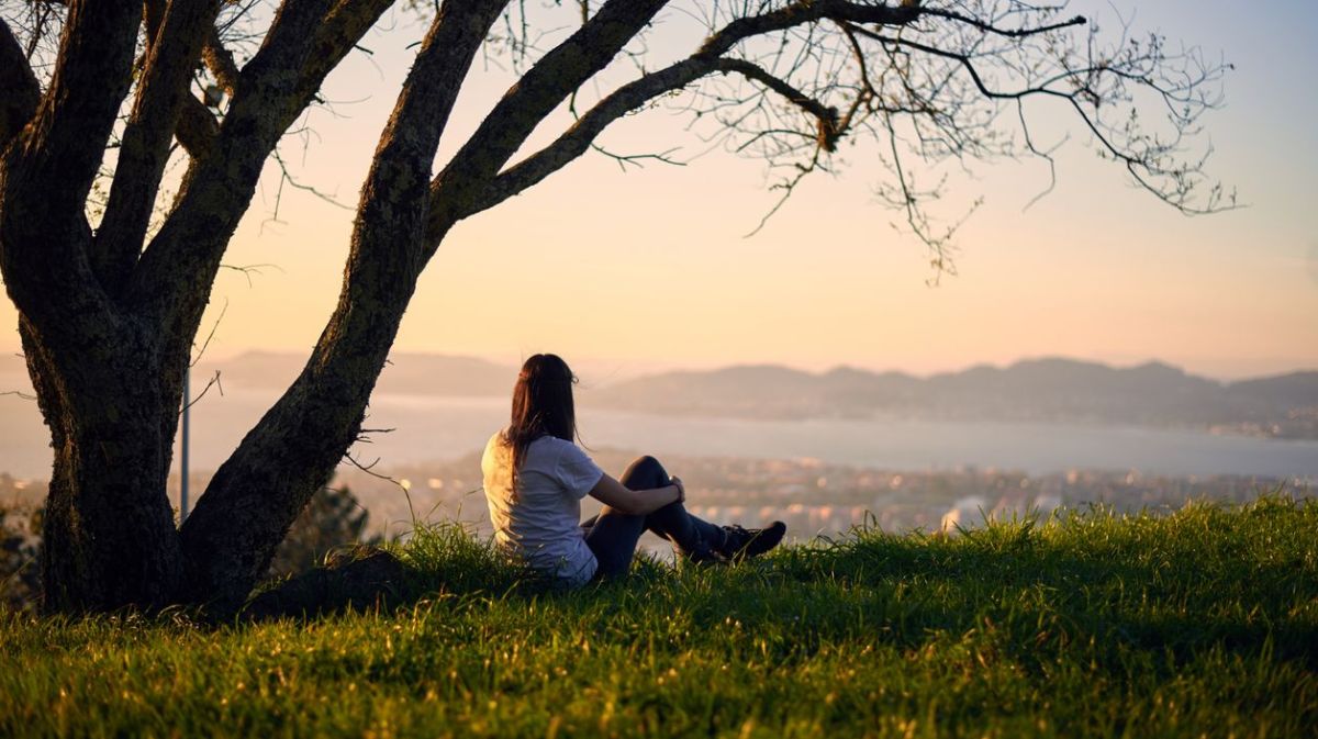 Frau sitzt alleine beim Sonnenuntergang unter einem Baum