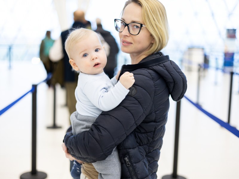 Mutter trägt ihr Baby auf dem Arm und beide stehen in der Schlange der Passkontrolle am Flughafen.