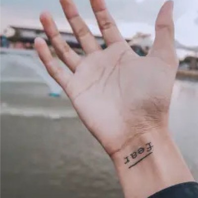 Hand mit dem Tattoo "Fear" am Handgelenk