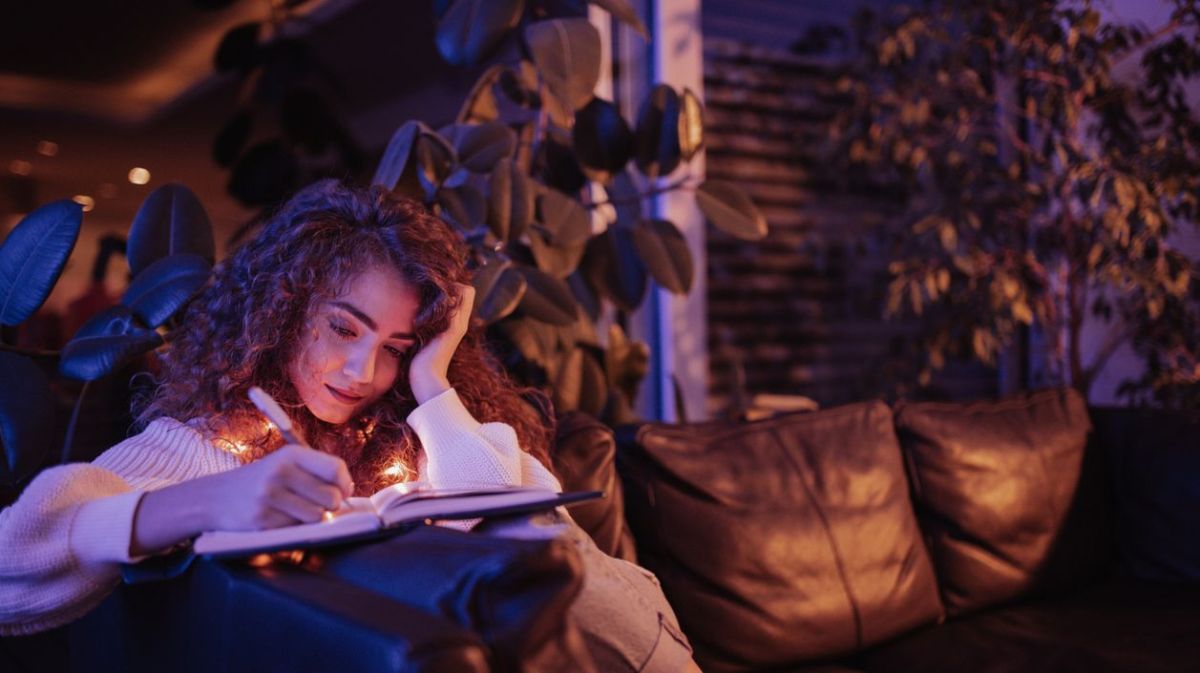 Frau sitzt in der Nacht auf dem Sofa und schreibt in ein Buch