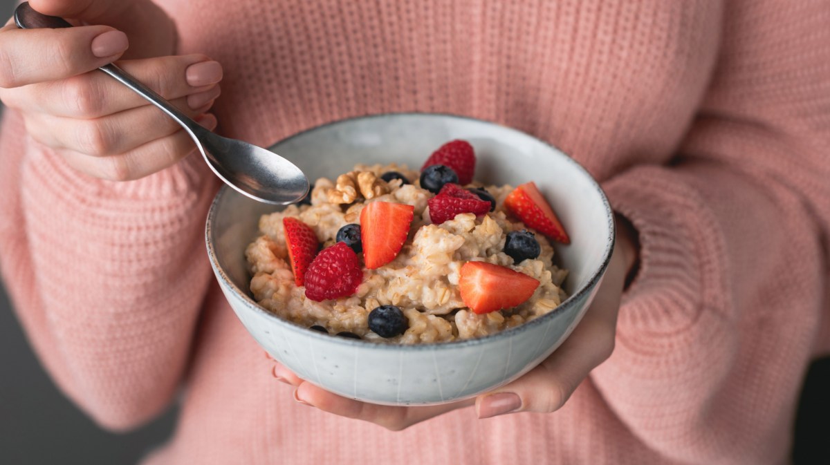 Frau mit rosa Pullover hält Schüssel mit Porridge und Früchten in Hand.