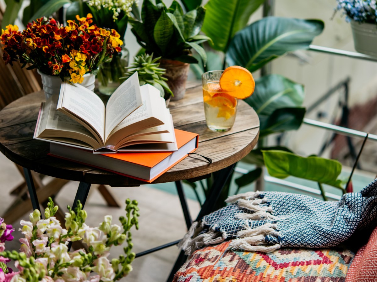 Balkon mit Accessoires, vielen Pflanzen und einem aufgeschlagenen Buch.