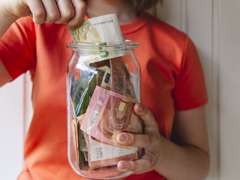 Frau wirft Bargeld in ein großes Glas.