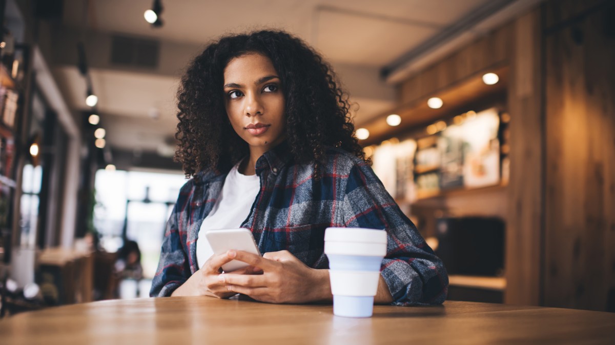 Frau sitzt nachdenklich in einem Café mit Handy in der Hand