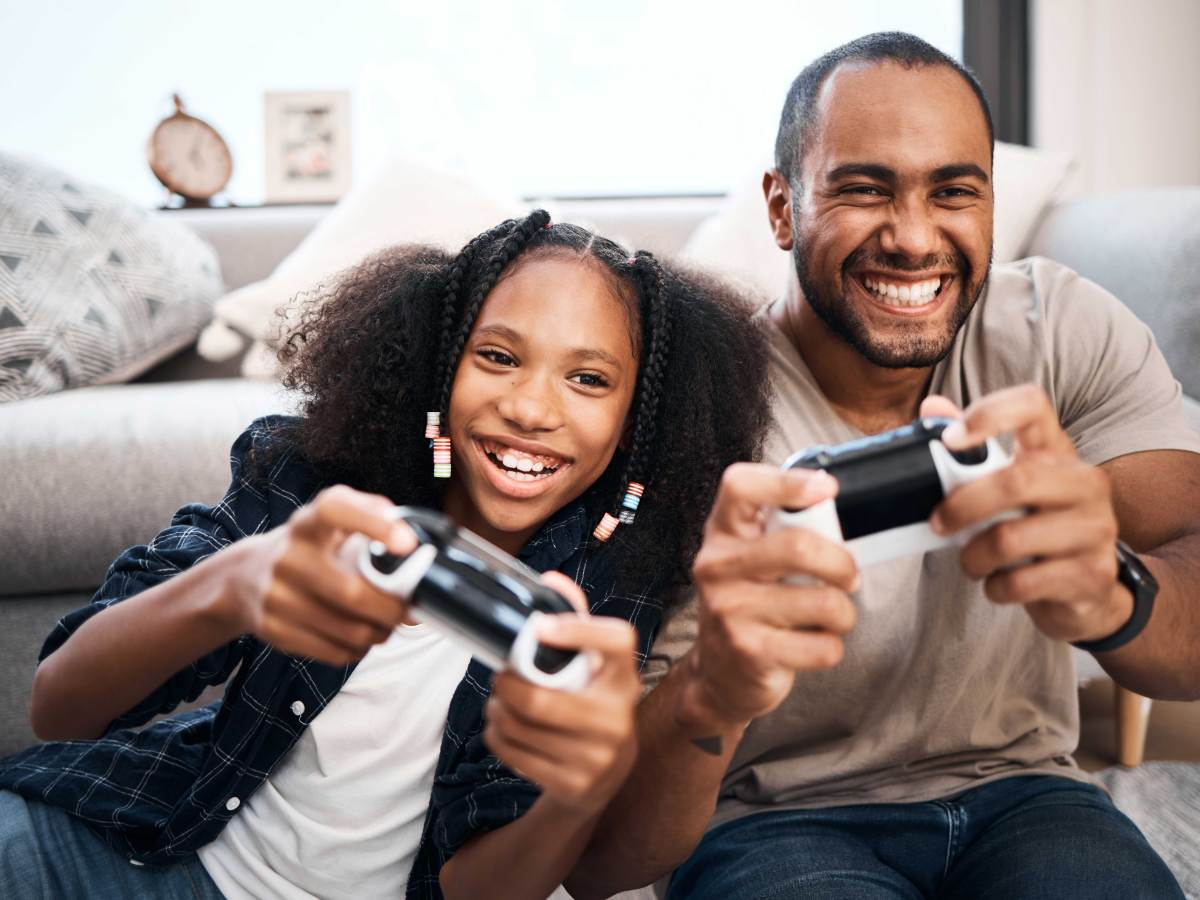 Vater und Tochter sitzen gemeinsam vor der Spielekonsole und zocken.