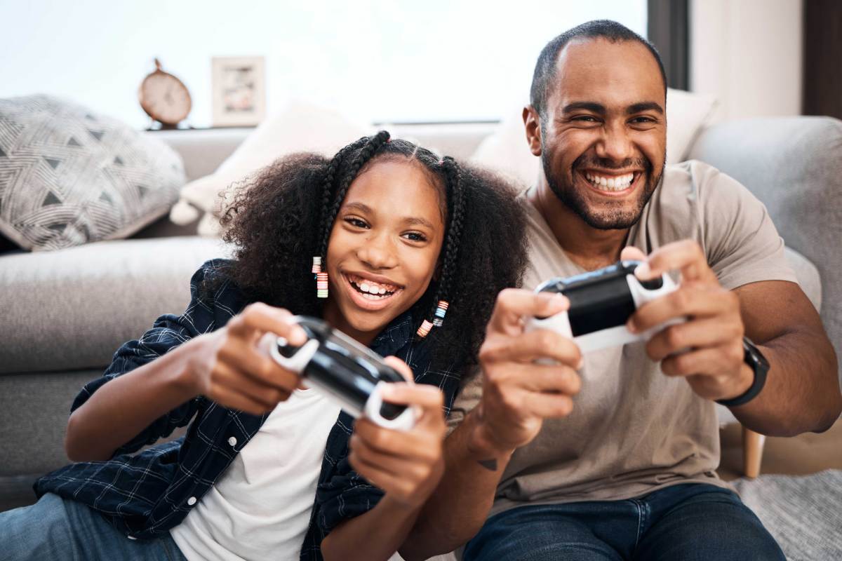 Vater und Tochter sitzen gemeinsam vor der Spielekonsole und zocken.