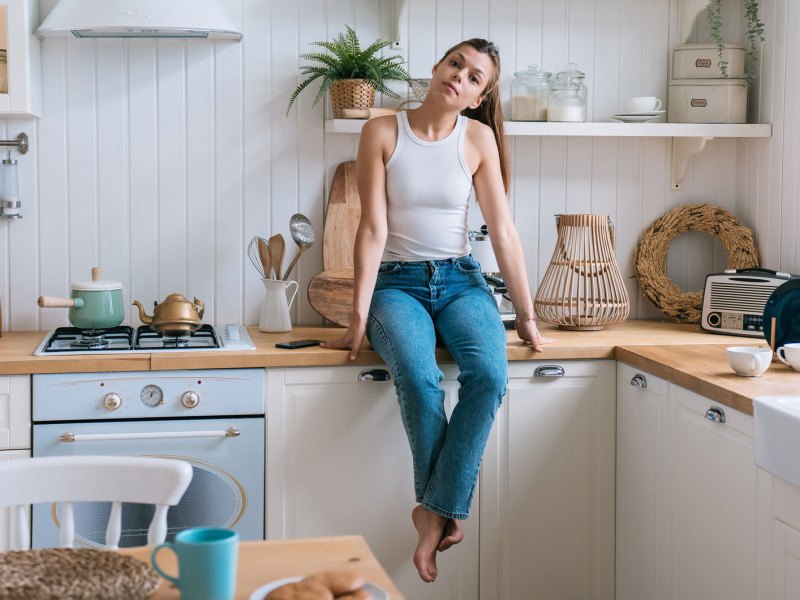 Junge Frau sitzt in ihrer rustikalen Küche auf der Küchenzeile.