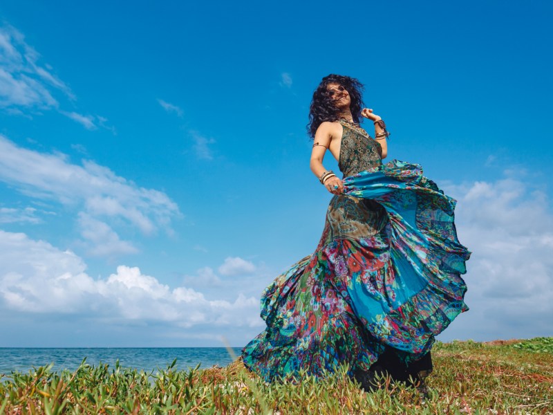 Frau tanzt in langem blauen Kleid auf einem Feld
