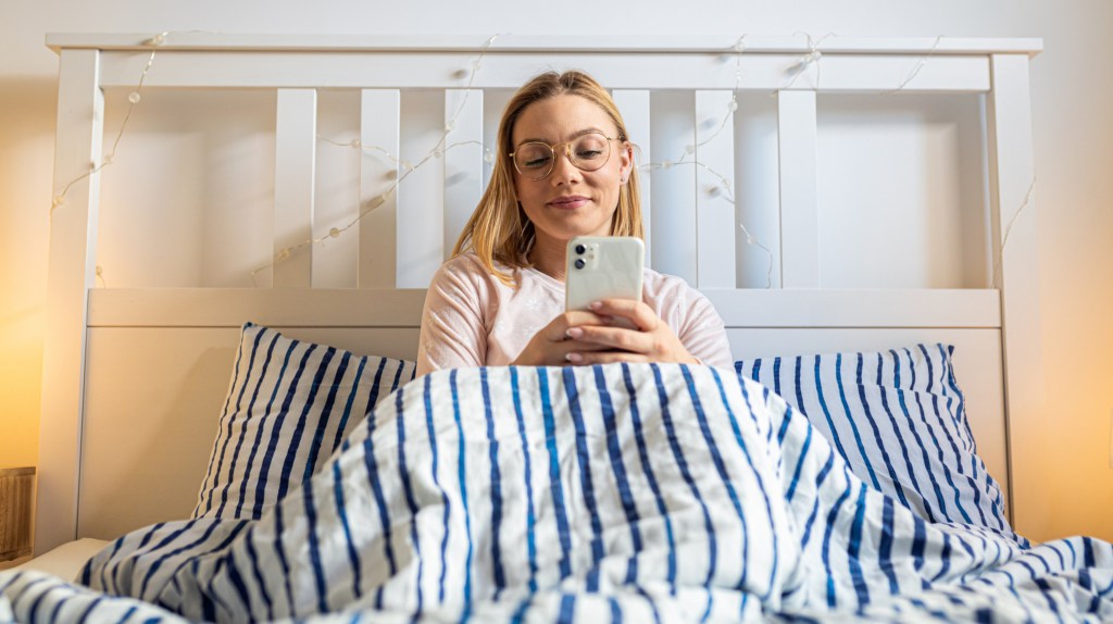 Frau benutzt Handy im Bett