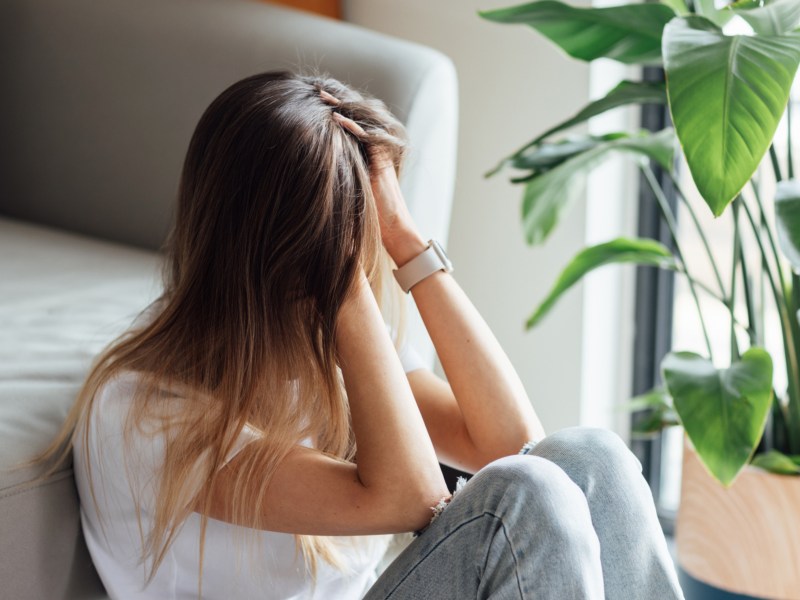 Frau sitzt vor Sofa und hält sich nachdenklich die Hände vors Gesicht