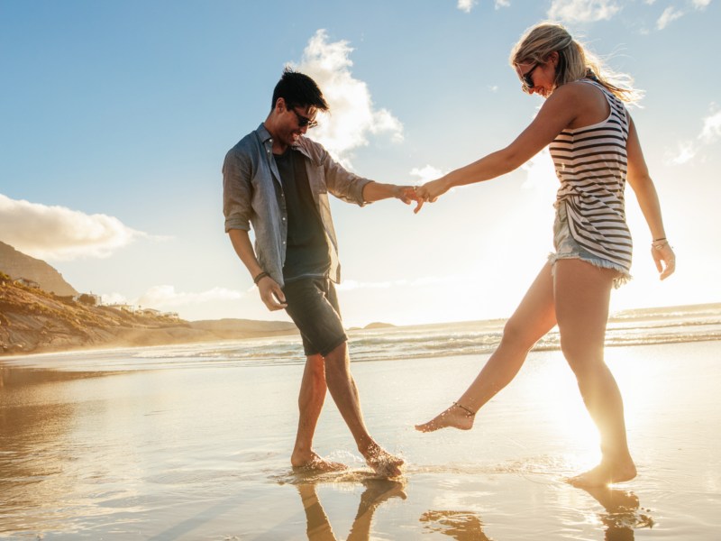 Pärchen am Strand hält sich an den Händen und tanzt