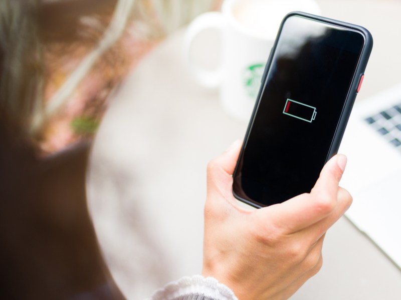 Eine Frau hält ein Handy in der Hand. Auf dem schwarzen Display sieht man das Symbol für einen leeren Akku.