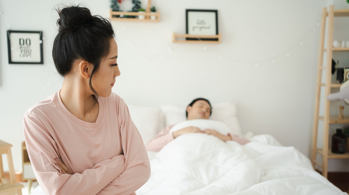 Frau schaut unzufrieden auf ihren Partner im Bett