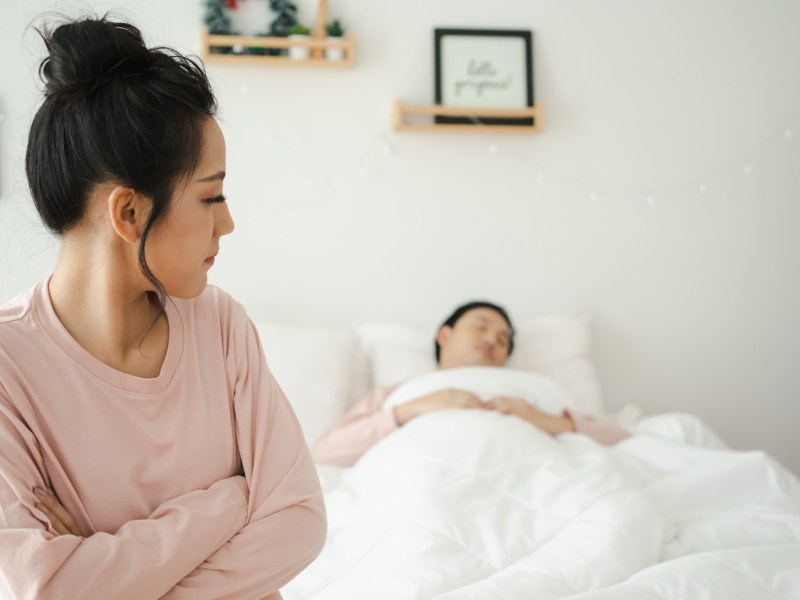 Frau schaut unzufrieden auf ihren Partner im Bett