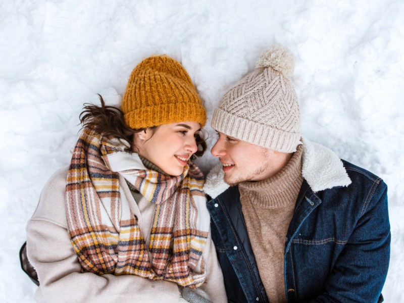 Pärchen, das gemeinsam im Schnee liegt und sich anlächelt