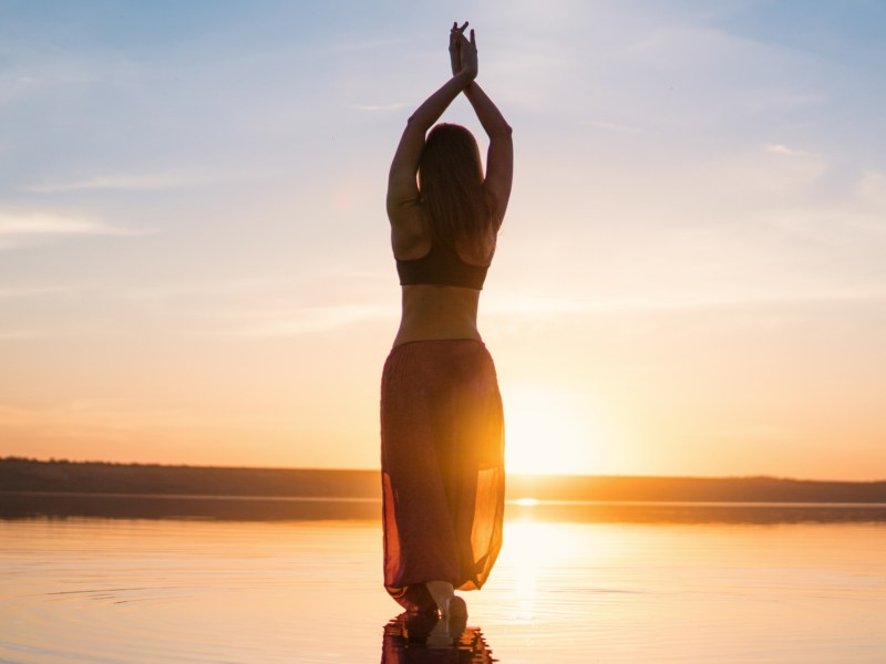 Frau macht Yoga am Strand während des Sonnenuntergangs
