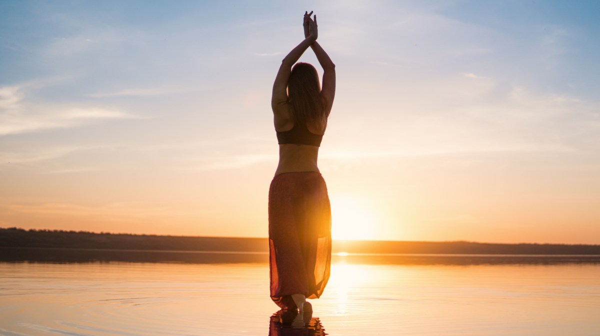 Frau macht Yoga am Strand während des Sonnenuntergangs