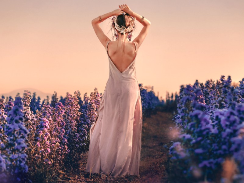 Frau steht im Blumenfeld, trägt langes Kleid.
