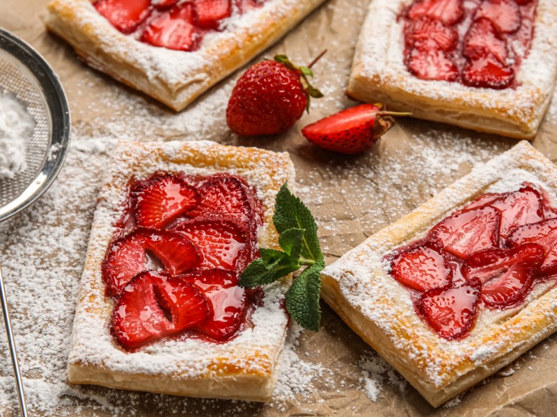 Blätterteig-Teilchen mit Erdbeeren und Puderzucker auf Backpapier.