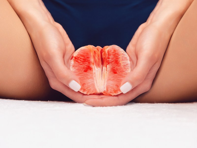 Hausmittel gegen Scheidenpilz: Frauenhände mit lackierten Fingernägeln halten eine Grapefruit zwischen den Beinen