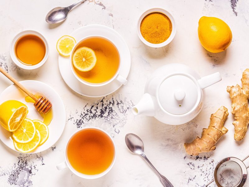 Hausmittel gegen Schleim im Hals wie Tee, Zitrone, Honig und Ingwer auf einem hellen Untergrund