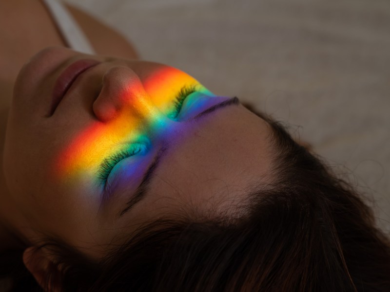 Frau liegt auf Boden, mit Regenbogenschimmer im Gesicht