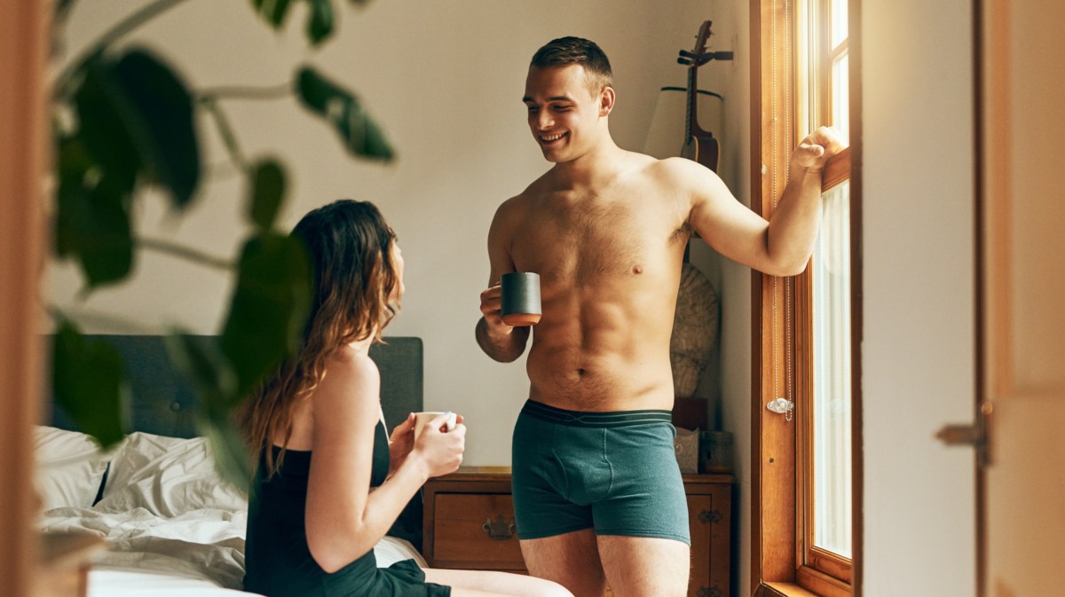 Frau und Mann in Unterwäsche vor Bett mit Kaffee in der Hand