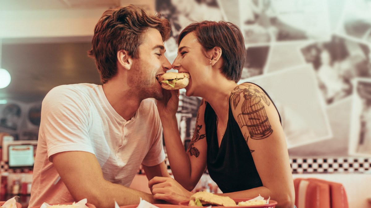 Mann und Frau beißen gleichzeitig in einen Burger hinein