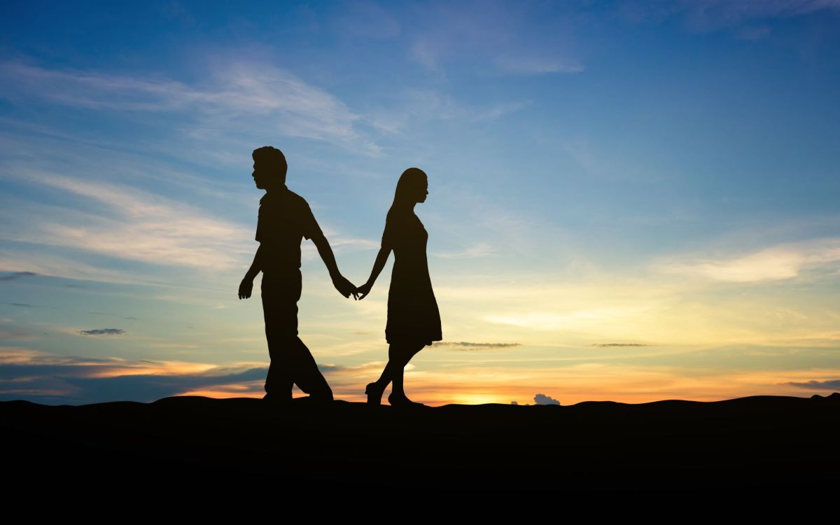 Silhouetten eines Paars das getrennte Wege geht vor Sonnenuntergang als Symbol für das Entlieben