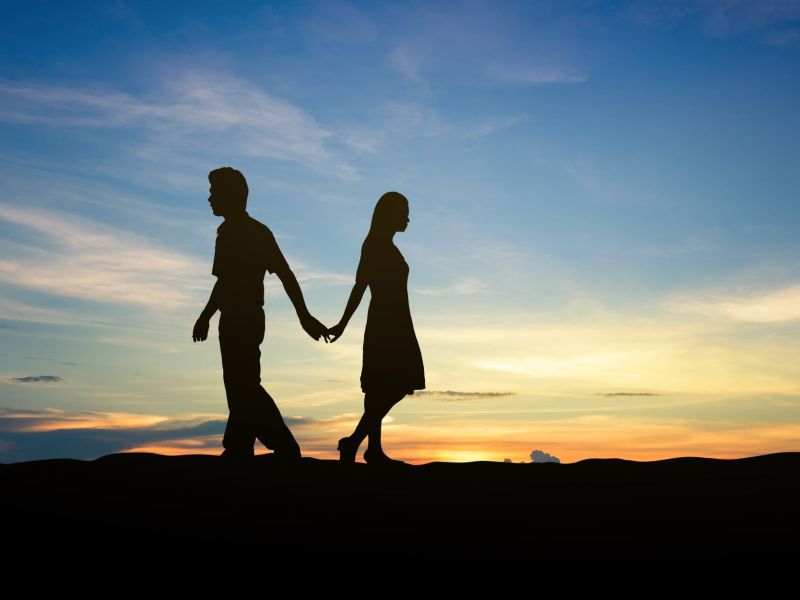 Silhouetten eines Paars das getrennte Wege geht vor Sonnenuntergang als Symbol für das Entlieben