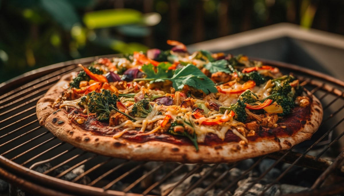 Pizza vom Grill belegt mit Kräutern, Käse und Gemüse.