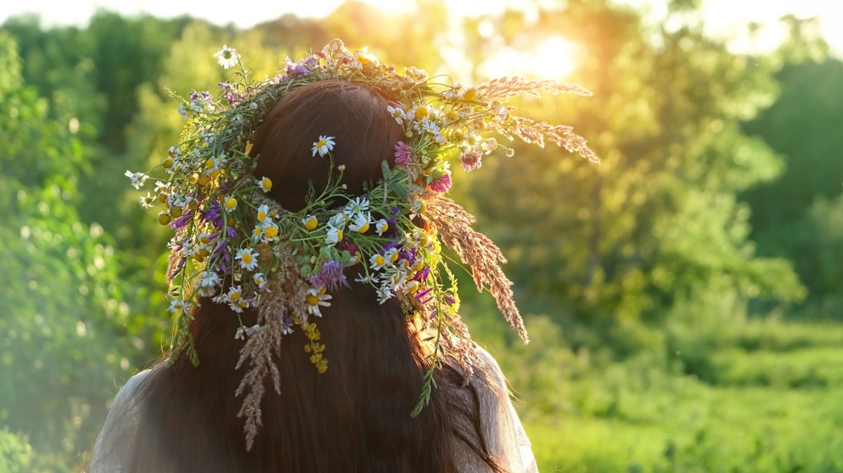 Frau mit Blumenkranz auf Kopf schaut zur Sonne.