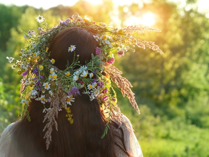 Frau mit Blumenkranz auf Kopf schaut zur Sonne.