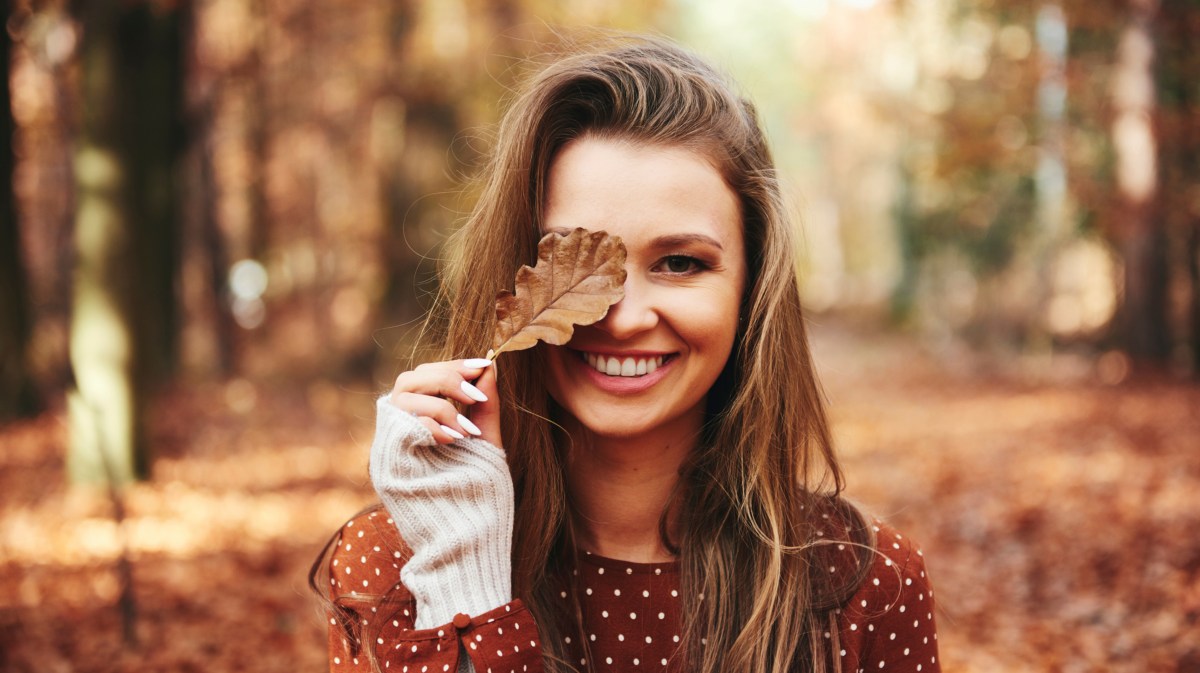 Frau hält Herbstblatt vor Gesicht.