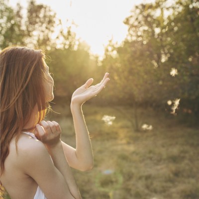 Red haired woman in forest area raises her hand towards the sun and enjoys nature