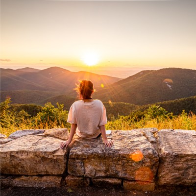 Frau, die auf einem Felsen sitzt und den Sonnenuntergang mit Landschaft bestaunt