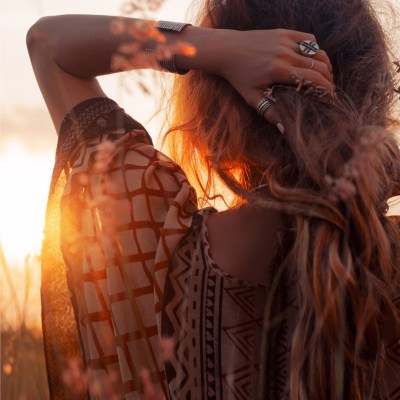 Woman dressed in boho clothing looks at the sunset while running her left hand through her hair