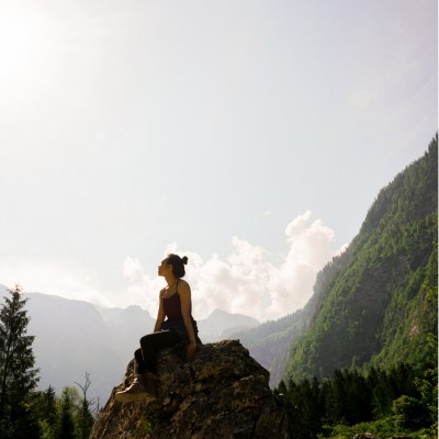 Woman on a rock in a mountainous area looking up at the sky