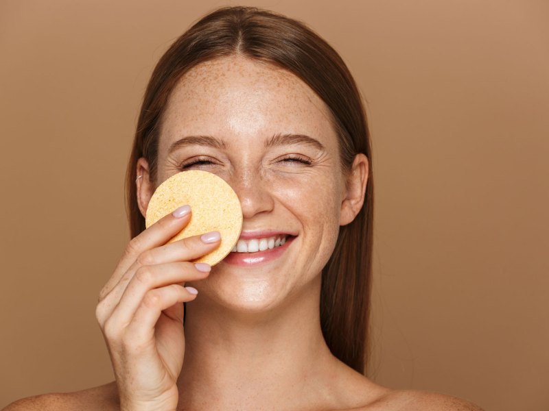 Frau, die mit einem Make-up-Schwamm eine Foundation aufträgt und dabei lacht.