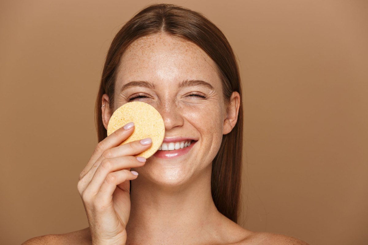 Frau, die mit einem Make-up-Schwamm eine Foundation aufträgt und dabei lacht.