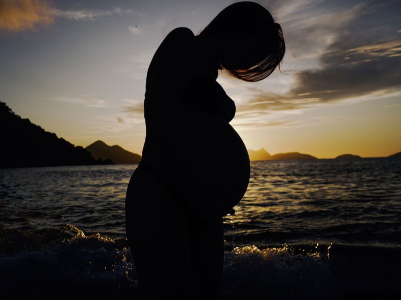 schwangere Frau vor einem Sonnenuntergang über dem Meer