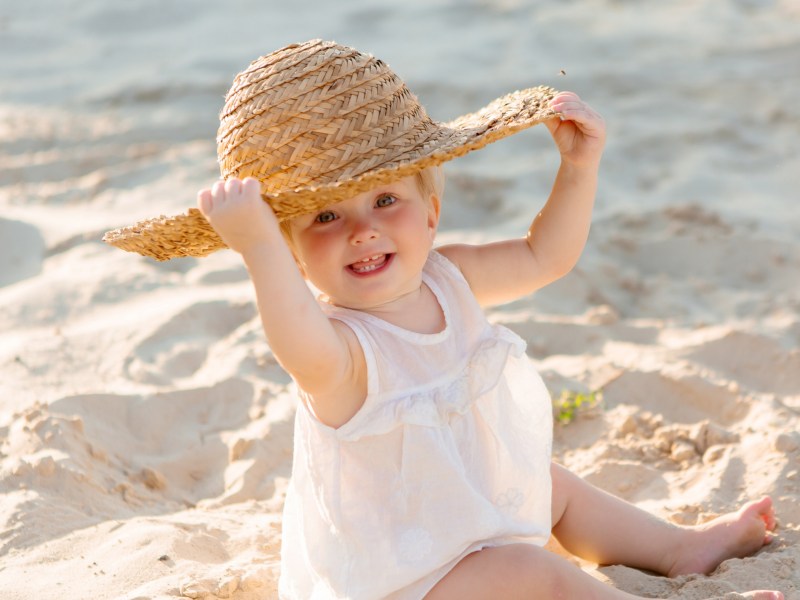 Baby am Strand mit Sonnenhut auf dem Kopf, das in die Kamera lächelt