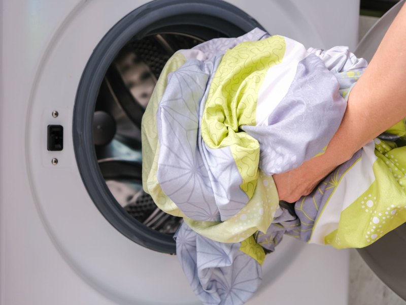 Hand mit Bettwäsche vor Waschmaschine